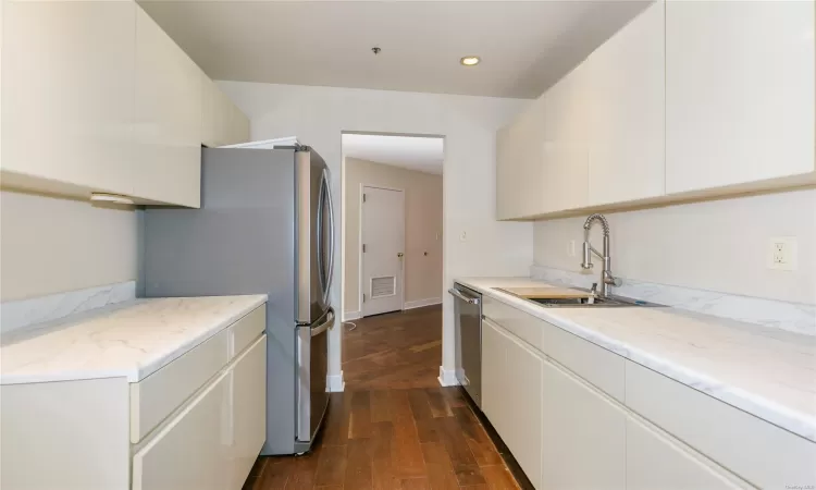 Kitchen with sink, appliances with stainless steel finishes, white cabinets, light stone counters, and dark wood-type flooring