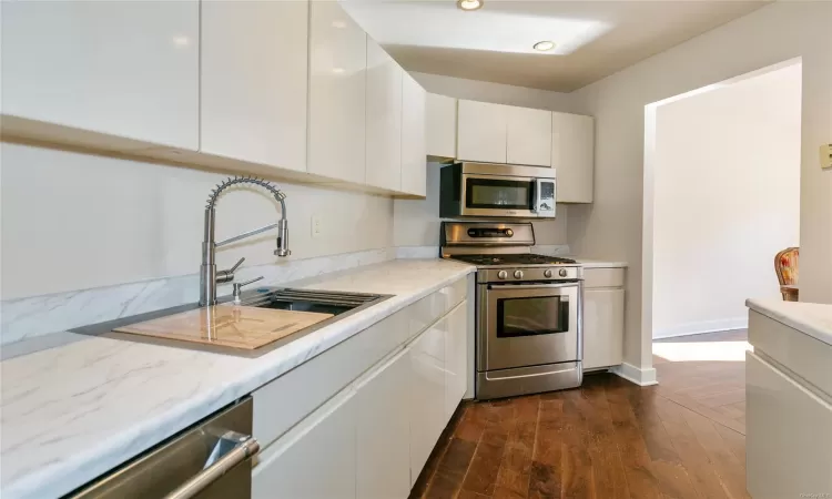 Kitchen with sink, white cabinetry, light stone counters, dark hardwood / wood-style floors, and appliances with stainless steel finishes