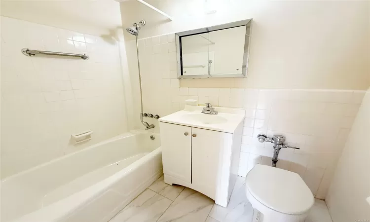 Full bathroom with tile walls, vanity, tiled shower / bath combo, and toilet