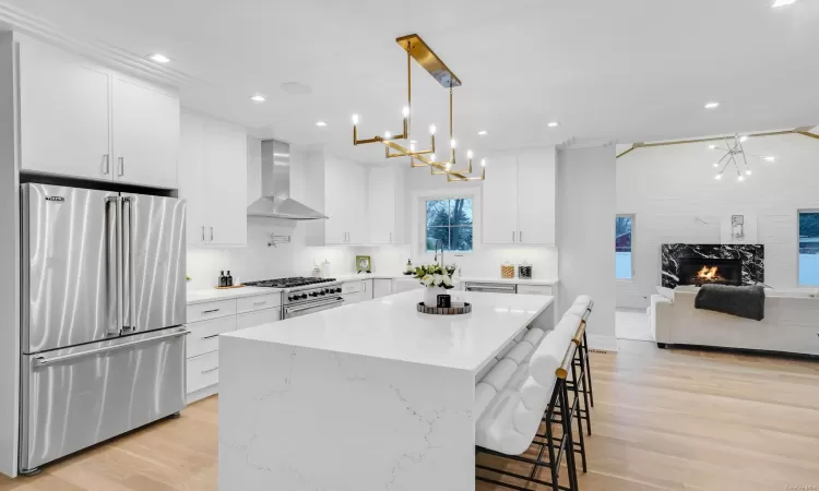 Kitchen with white cabinets, wall chimney exhaust hood, high end appliances, and hanging light fixtures