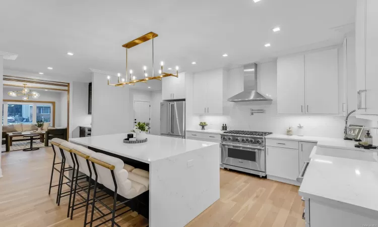 Kitchen featuring high end appliances, white cabinets, hanging light fixtures, wall chimney exhaust hood, and a kitchen island