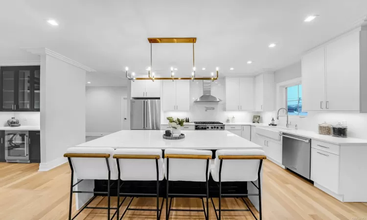 Kitchen with a center island, white cabinets, wall chimney range hood, sink, and appliances with stainless steel finishes