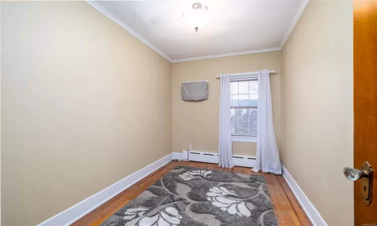 Empty room featuring ornamental molding, a baseboard heating unit, and hardwood / wood-style flooring