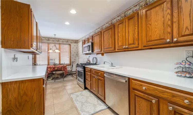 Kitchen featuring sink, a baseboard radiator, decorative light fixtures, light tile patterned floors, and appliances with stainless steel finishes