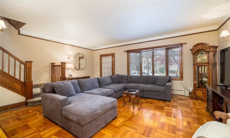 Living room with baseboard heating, parquet floors, and crown molding