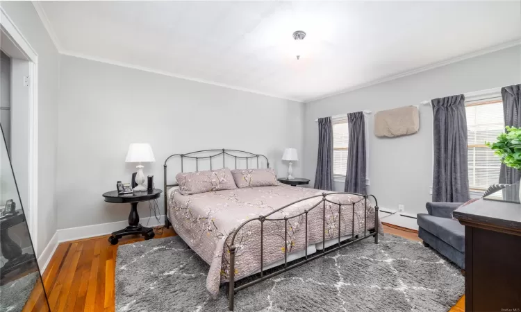 Bedroom with wood-type flooring, a baseboard heating unit, and ornamental molding