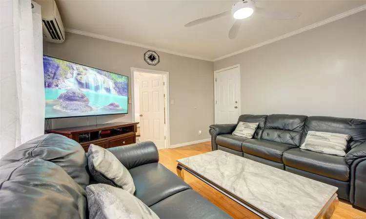 Living room featuring a wall mounted AC, crown molding, ceiling fan, and light wood-type flooring