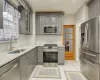 Kitchen with light stone countertops, appliances with stainless steel finishes, gray cabinetry, sink, and light tile patterned floors