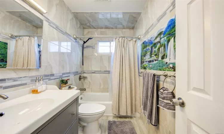 Full bathroom with vanity, toilet, shower / bathtub combination with curtain, and tile walls