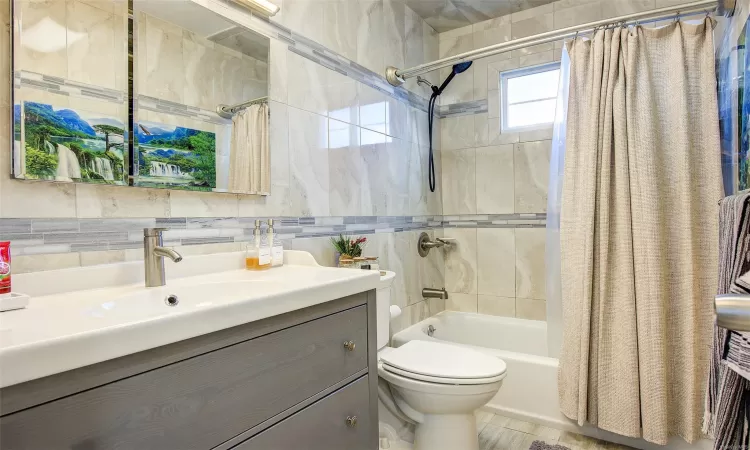 Full bathroom featuring vanity, shower / tub combo, tile walls, and toilet