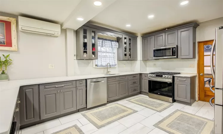 Kitchen with a wall mounted AC, sink, gray cabinetry, and appliances with stainless steel finishes