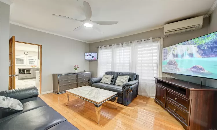 Living room featuring light hardwood / wood-style floors, a wall unit AC, ceiling fan, and crown molding