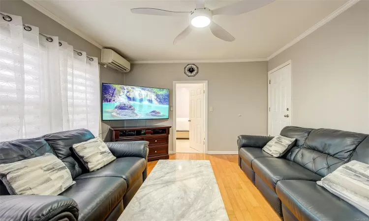 Living room with hardwood / wood-style flooring, ceiling fan, ornamental molding, and a wall mounted AC