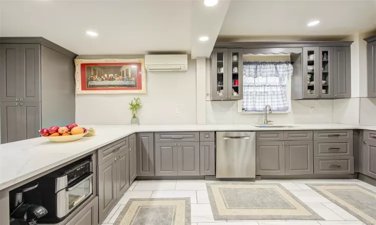 Kitchen featuring a wall mounted air conditioner, dishwasher, gray cabinetry, and sink