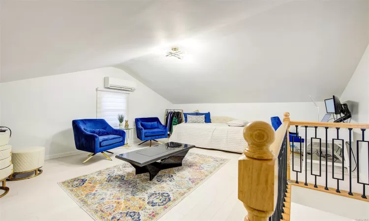 Living area with a wall mounted AC, wood-type flooring, and lofted ceiling