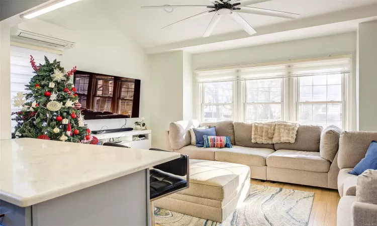 Living room with an AC wall unit, ceiling fan, lofted ceiling, and light wood-type flooring