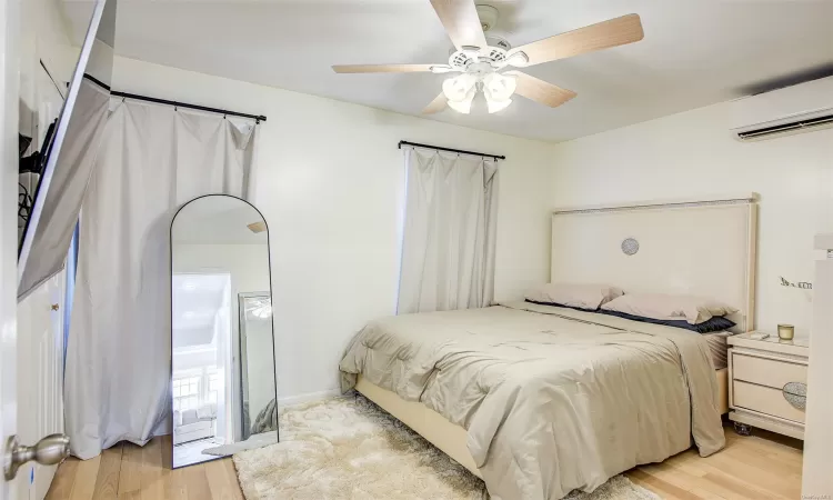 Bedroom featuring a wall unit AC, ceiling fan, and light hardwood / wood-style flooring