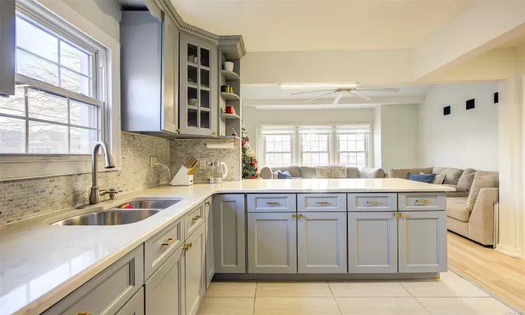 Kitchen featuring kitchen peninsula, light wood-type flooring, backsplash, sink, and gray cabinets