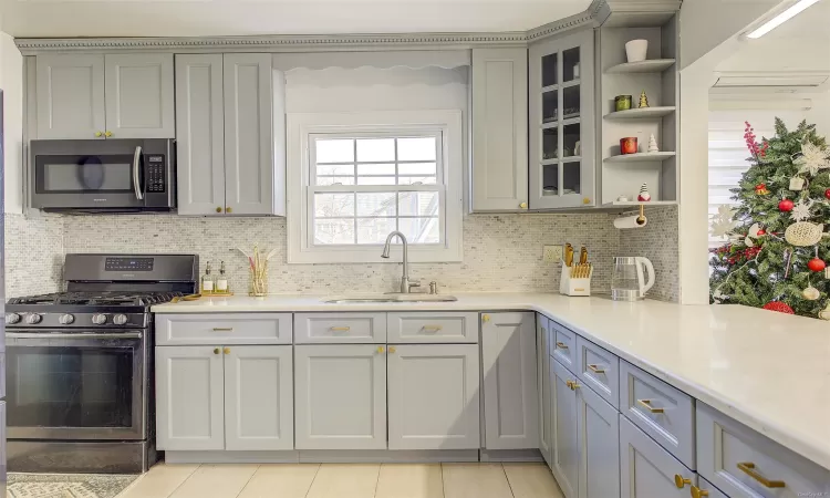 Kitchen featuring backsplash, stainless steel appliances, gray cabinetry, and sink