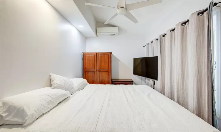 Bedroom featuring ceiling fan, an AC wall unit, and vaulted ceiling