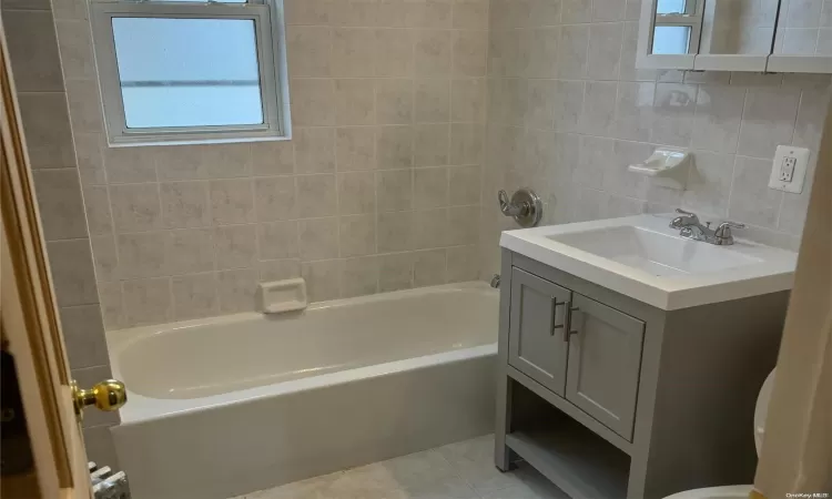 Full bathroom featuring vanity, tile walls, tile patterned flooring, radiator heating unit, and tiled shower / bath