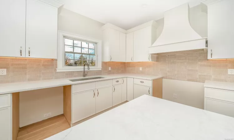 Kitchen featuring white cabinets, custom range hood, and sink