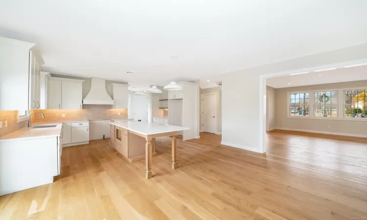 Kitchen featuring light wood-type flooring, premium range hood, sink, white cabinets, and a center island