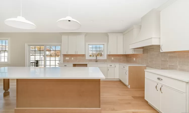 Kitchen featuring custom range hood, pendant lighting, white cabinetry, and a kitchen island