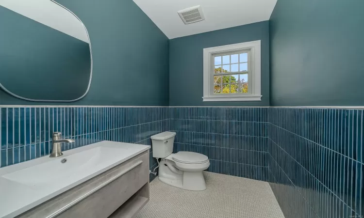 Bathroom featuring tile patterned floors, vanity, toilet, and tile walls