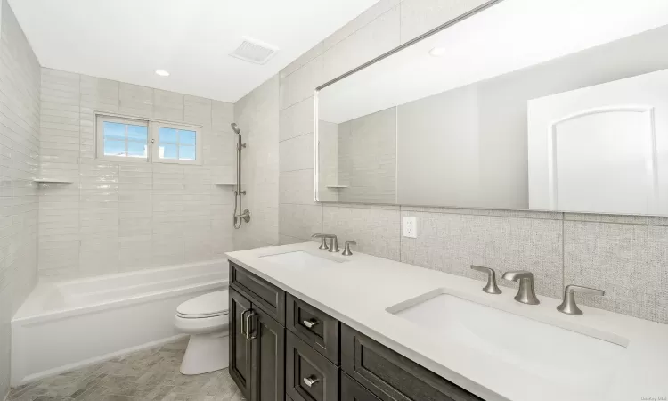 Full bathroom featuring decorative backsplash, vanity, tile walls, toilet, and tiled shower / bath