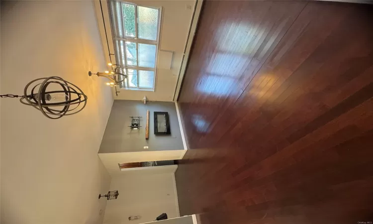 Unfurnished living room with a baseboard radiator, an inviting chandelier, and dark wood-type flooring