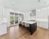 Kitchen with white cabinets, an island with sink, light hardwood / wood-style floors, and wall chimney range hood