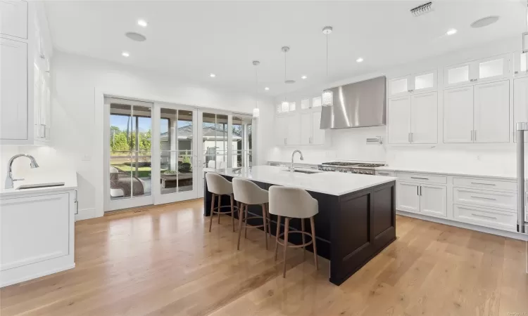 Kitchen with white cabinets, an island with sink, light hardwood / wood-style floors, and wall chimney range hood