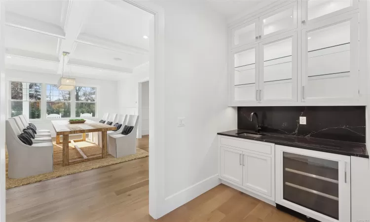 Bar with backsplash, white cabinets, sink, wine cooler, and light wood-type flooring