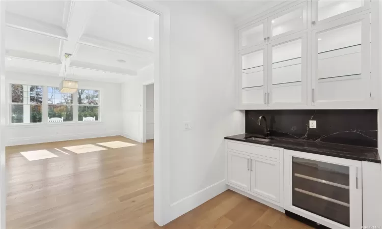 Bar featuring wine cooler, sink, white cabinets, and light hardwood / wood-style floors