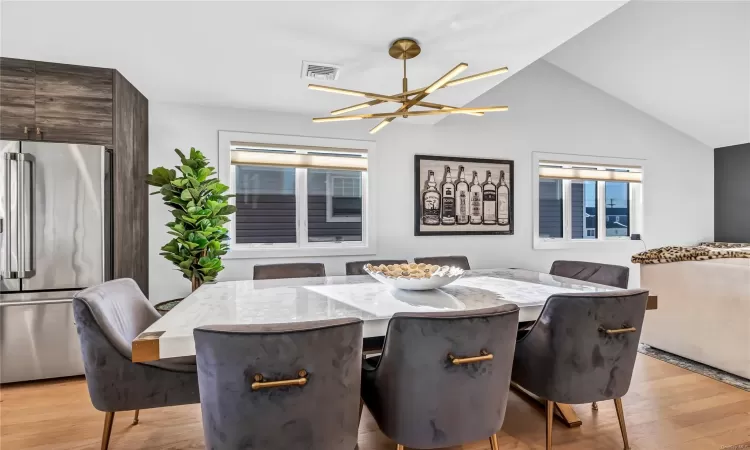 Dining space with an inviting chandelier, light wood-type flooring, and vaulted ceiling