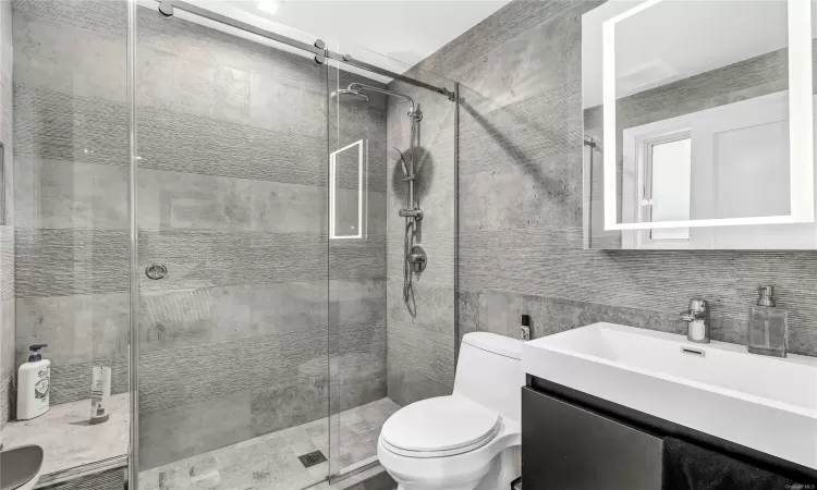 Bathroom with vanity, a shower with door, toilet, tile walls, and tasteful backsplash