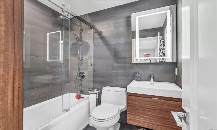 Full bathroom with combined bath / shower with glass door, backsplash, vanity, tile walls, and toilet