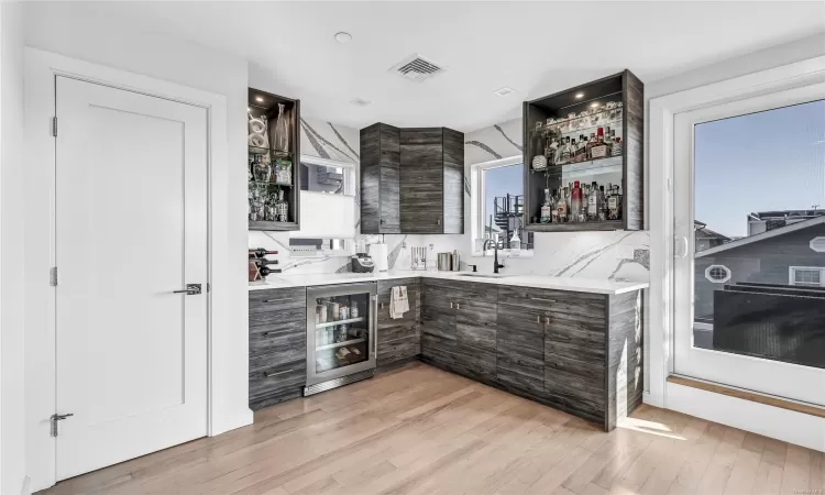 Bar featuring sink, beverage cooler, tasteful backsplash, light hardwood / wood-style flooring, and dark brown cabinets