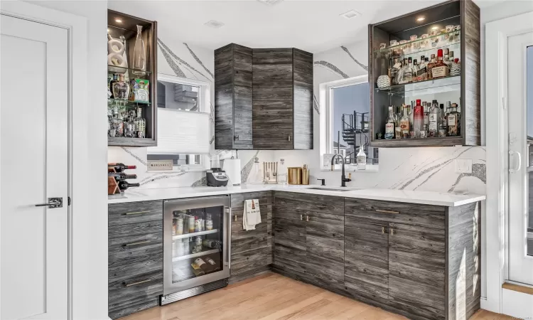 Bar with sink, beverage cooler, light hardwood / wood-style flooring, backsplash, and dark brown cabinets