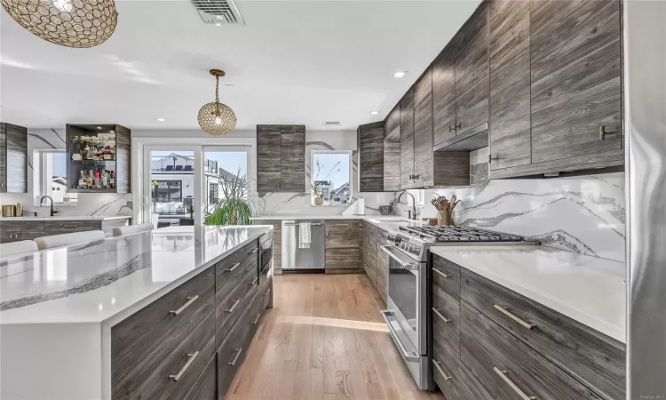 Kitchen featuring light wood-type flooring, decorative light fixtures, stainless steel appliances, and sink