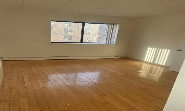 Unfurnished room featuring baseboard heating, a paneled ceiling, and light wood-type flooring