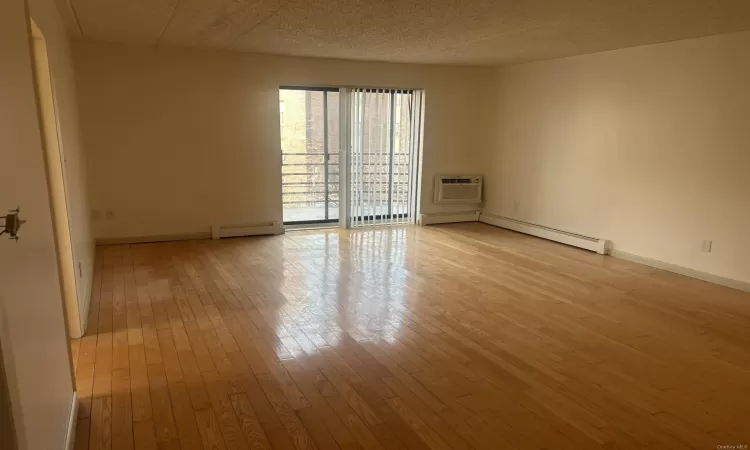 Unfurnished room featuring a wall mounted air conditioner, a textured ceiling, a baseboard radiator, and light hardwood / wood-style floors