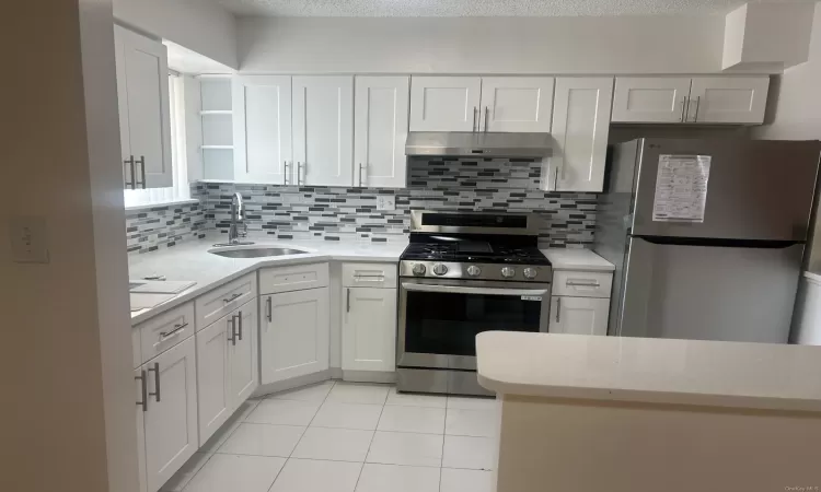 Kitchen featuring appliances with stainless steel finishes, tasteful backsplash, a textured ceiling, sink, and white cabinetry