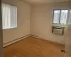 Empty room with a wall mounted air conditioner, a baseboard heating unit, and light hardwood / wood-style flooring