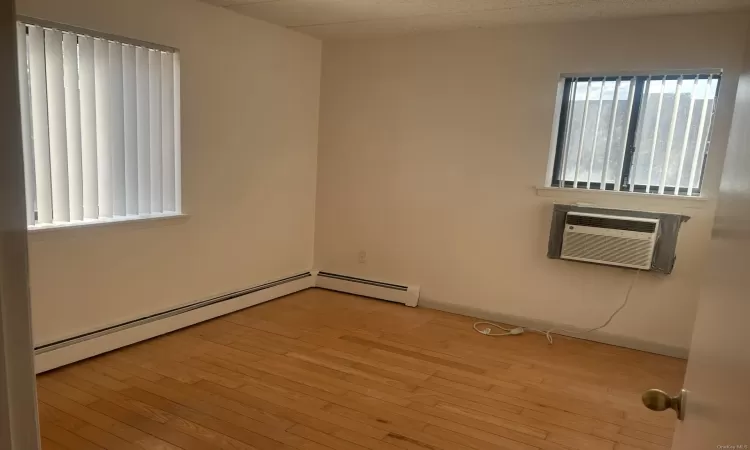 Empty room with a wall mounted air conditioner, a baseboard heating unit, and light hardwood / wood-style flooring