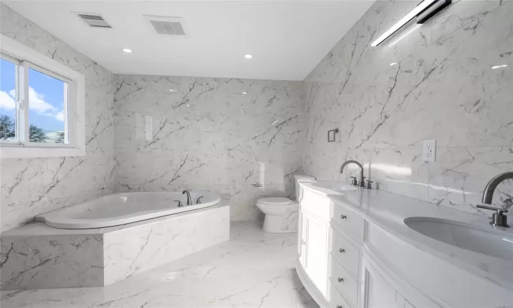 Bathroom featuring a bath, vanity, toilet, and tile walls