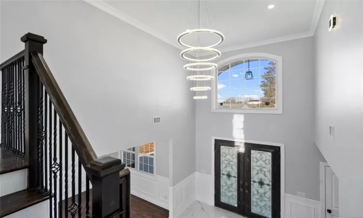 Foyer with french doors, an inviting chandelier, and crown molding