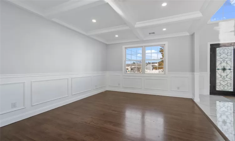 Empty room featuring dark hardwood / wood-style floors, beam ceiling, crown molding, and coffered ceiling