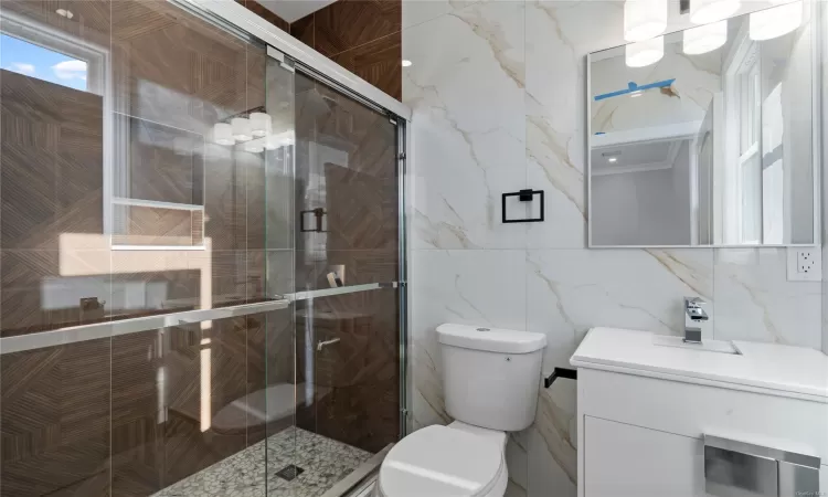 Bathroom featuring toilet, a shower with shower door, and tile walls